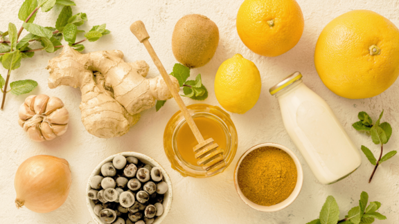 Flatlay von Ingwer, Zitrone, Orange, Honig, Minze und Knoblauch auf hellem Grund